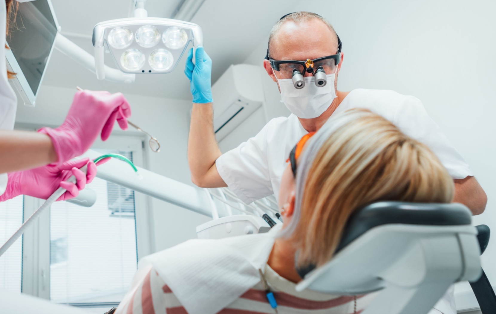 A dentist prepares to start a root canal procedure on a patient while a dental assistant stands to the side.