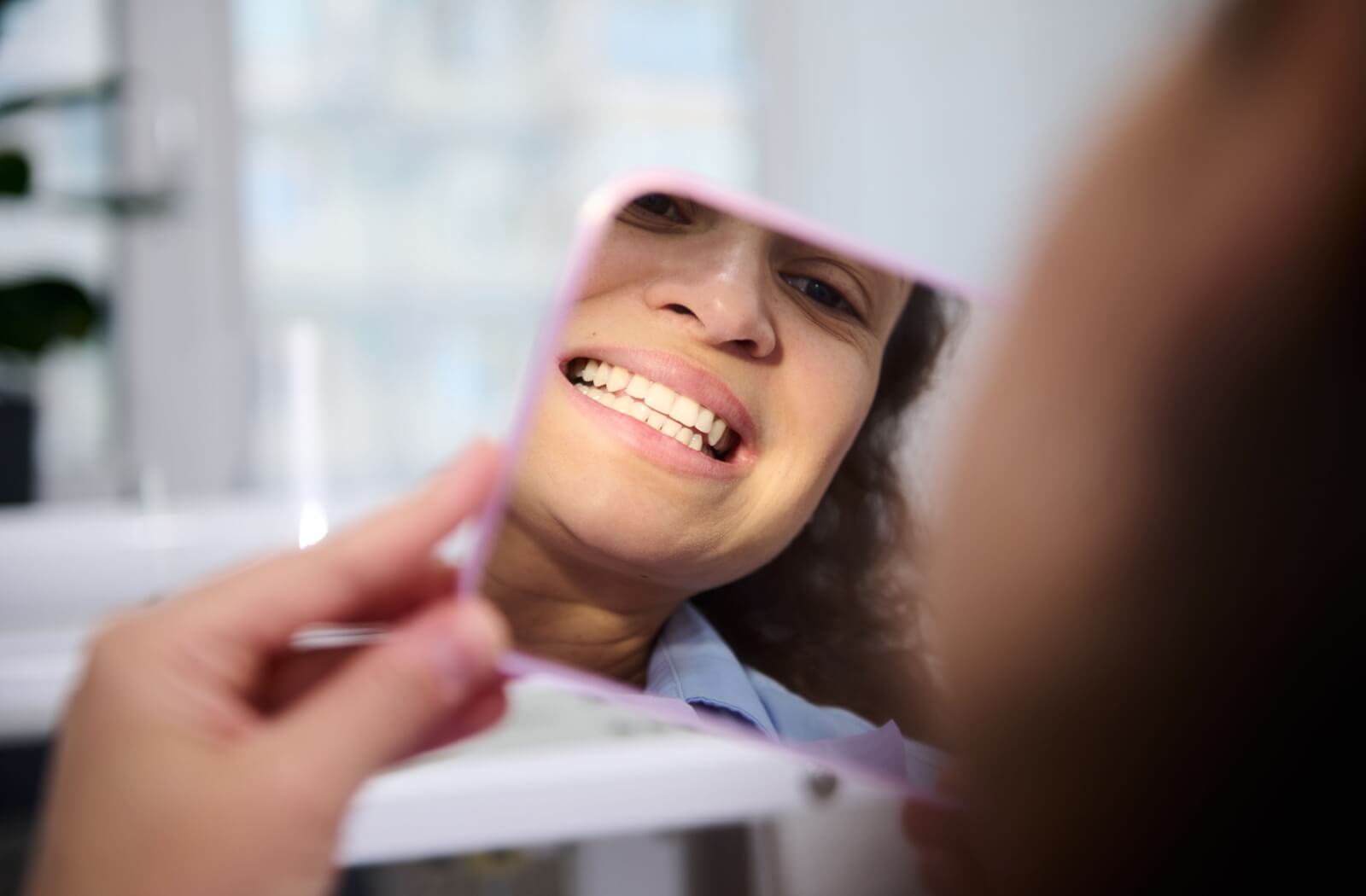 A dental patient smiles into a pink-framed mirror to see their chipped tooth has been fixed with fillings